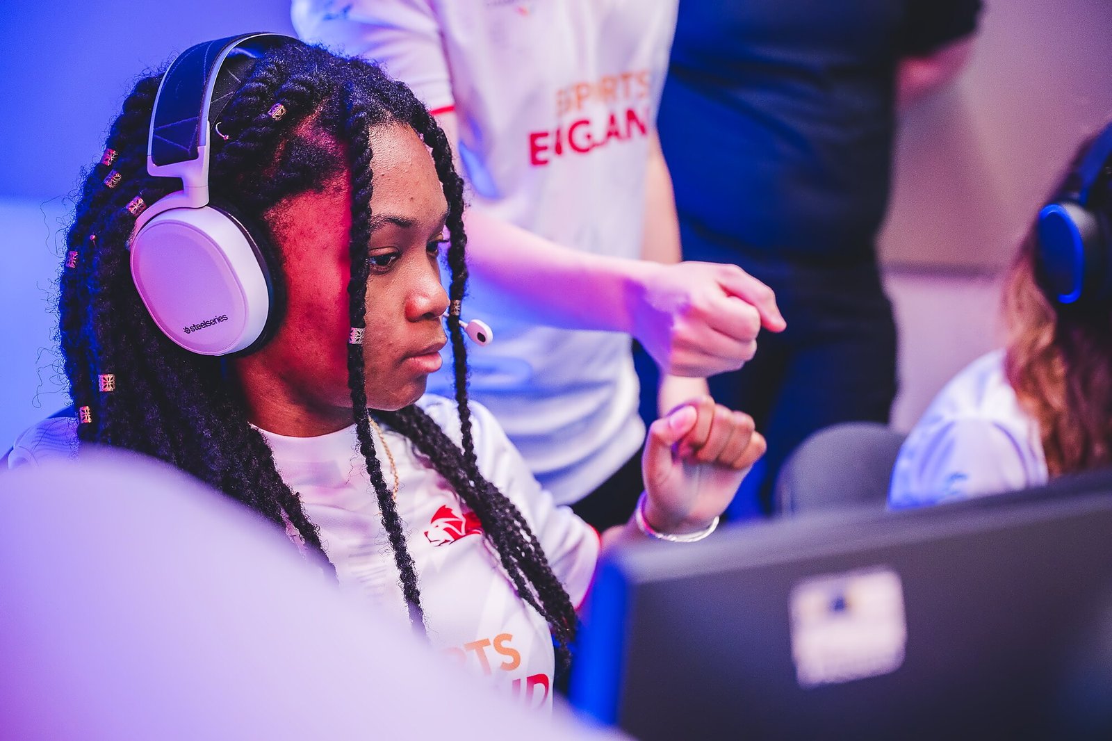 Alanis at her PC in the Team England shirt, sharing a fist bump with a teammate